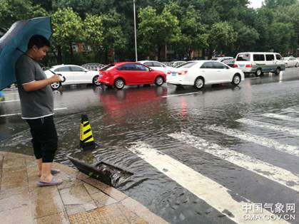 北京7月17日清晨，石景山古城附近，北京排水集团工作人员打开排水口，并提醒路人注意。路面略有积水，车辆行动减缓。申敏夏 摄.jpg